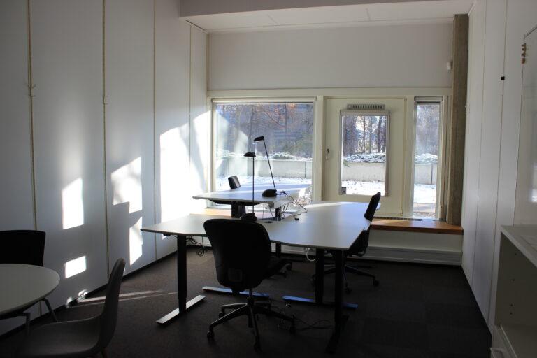 Three-person office with sit-stand desks and windows facing greenery